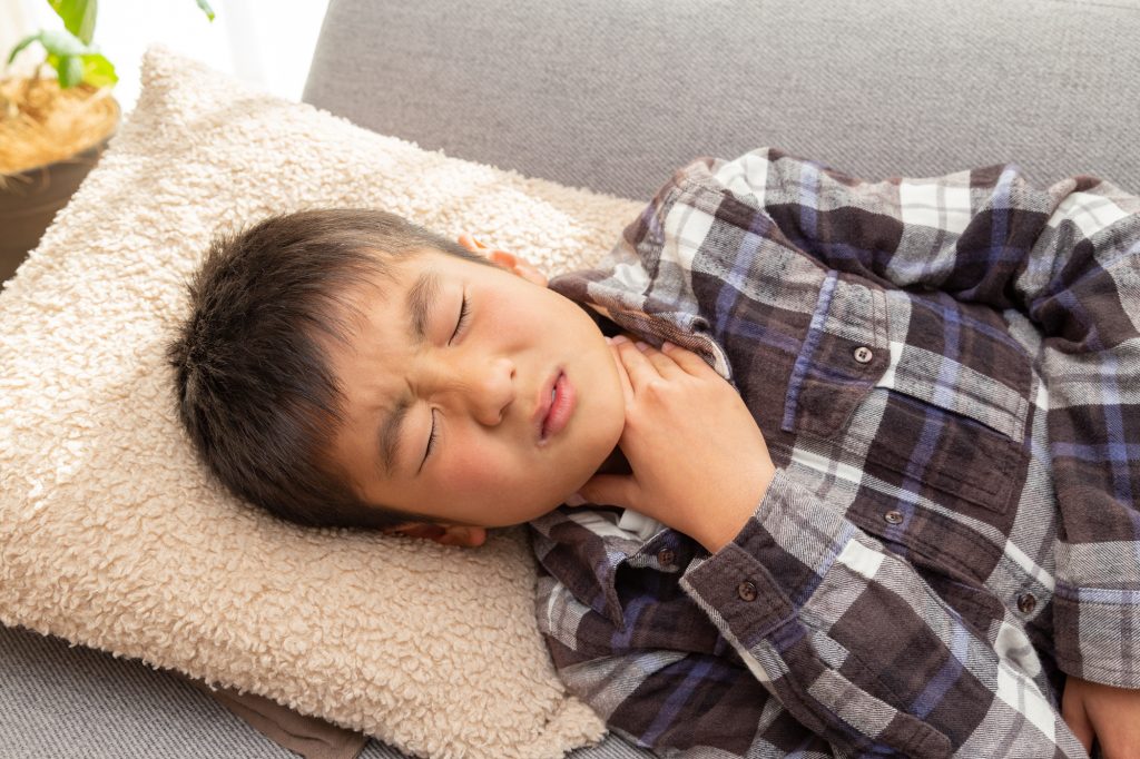 のど元に手を当て辛そうな表情の男の子