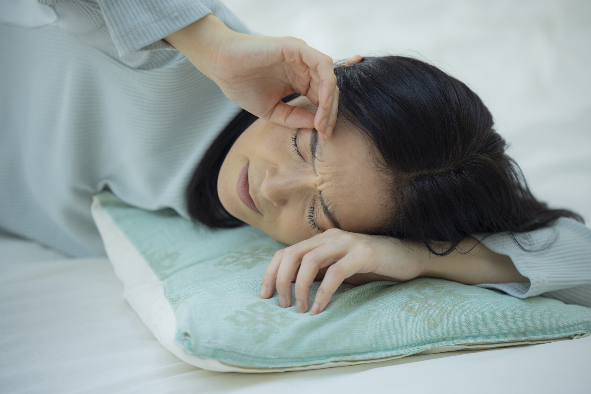 横になりながらこめかみを押さえる女性