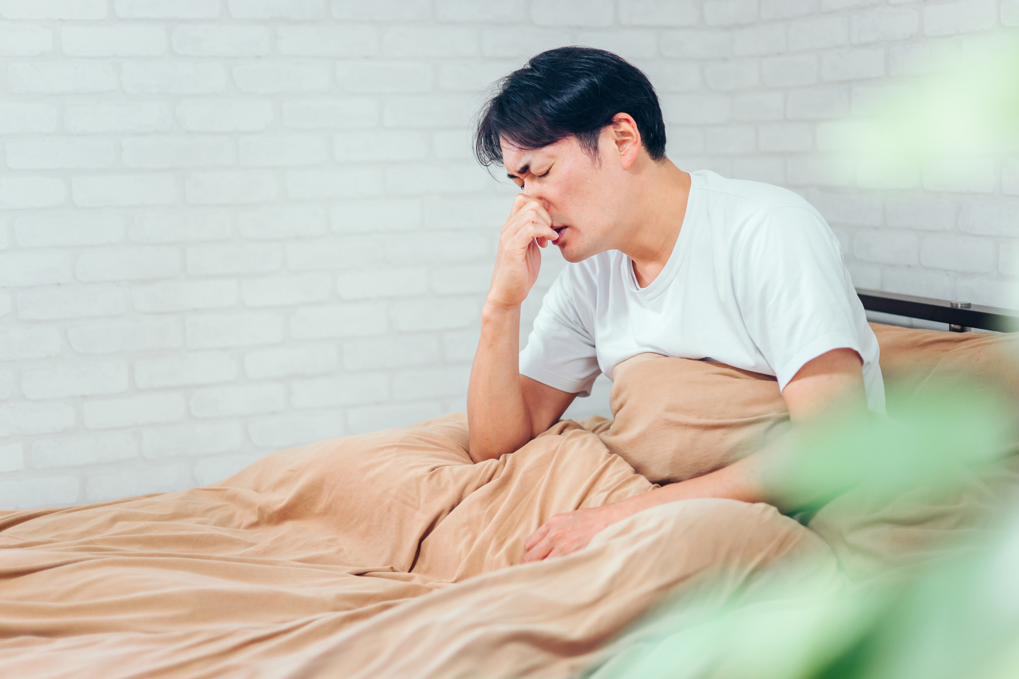 ベッドに座り鼻を押さえる男性