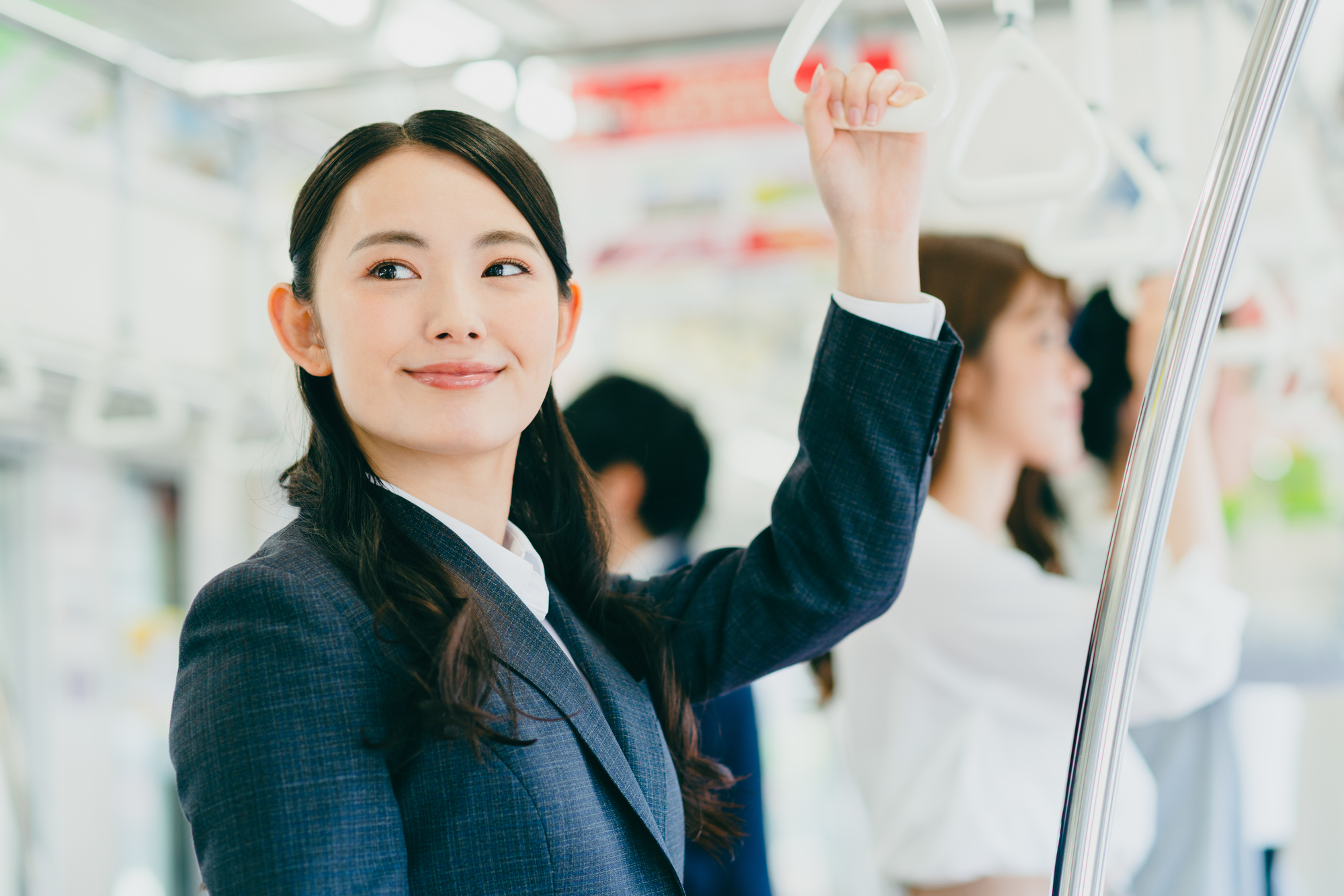 電車の吊革につかまり、微笑みを浮かべている若い女性